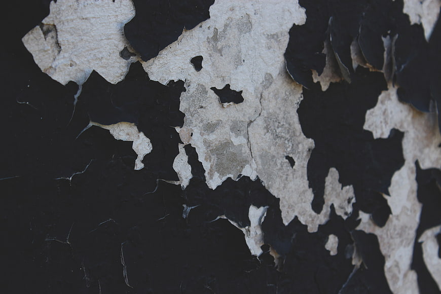 Close-up of peeling black paint on a textured concrete wall