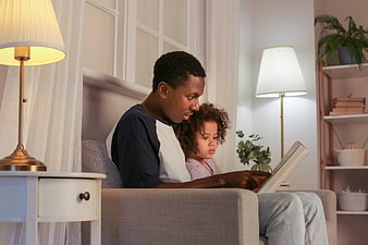 Father reading book to daughter on sofa at home