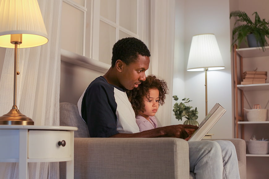 Father reading book to daughter on sofa at home