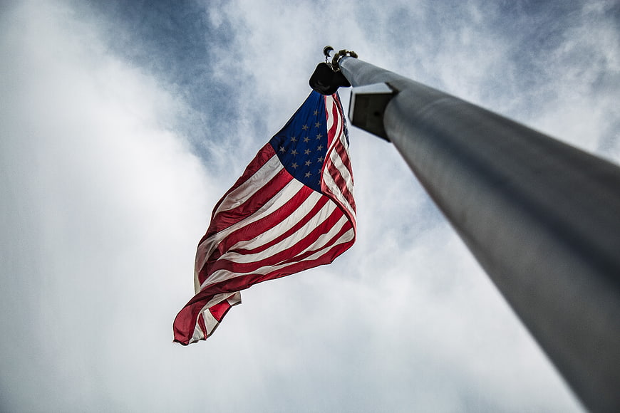 Low angle view of American flag waving against cloudy sky