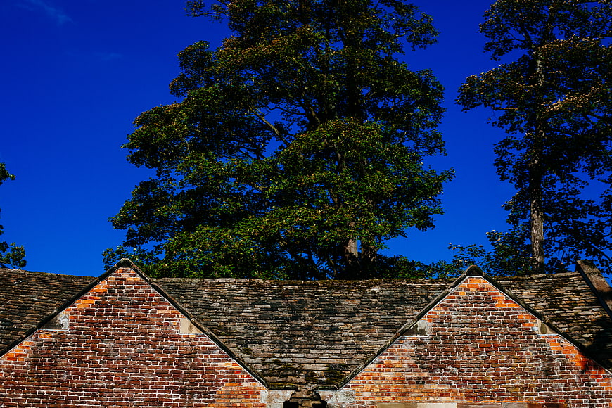 Old brick roof with slate tiles against blue sky and trees