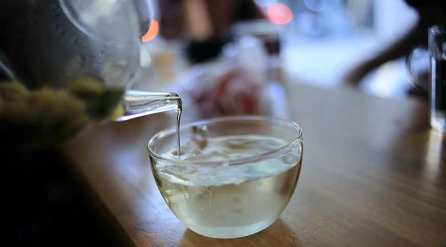 Pouring Clear Tea into Glass Cup on Wooden Table