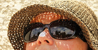 Close-up of woman wearing straw hat and sunglasses with sunscreen on nose
