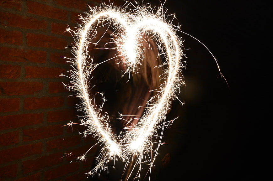Sparkler heart shape light painting against dark red brick wall