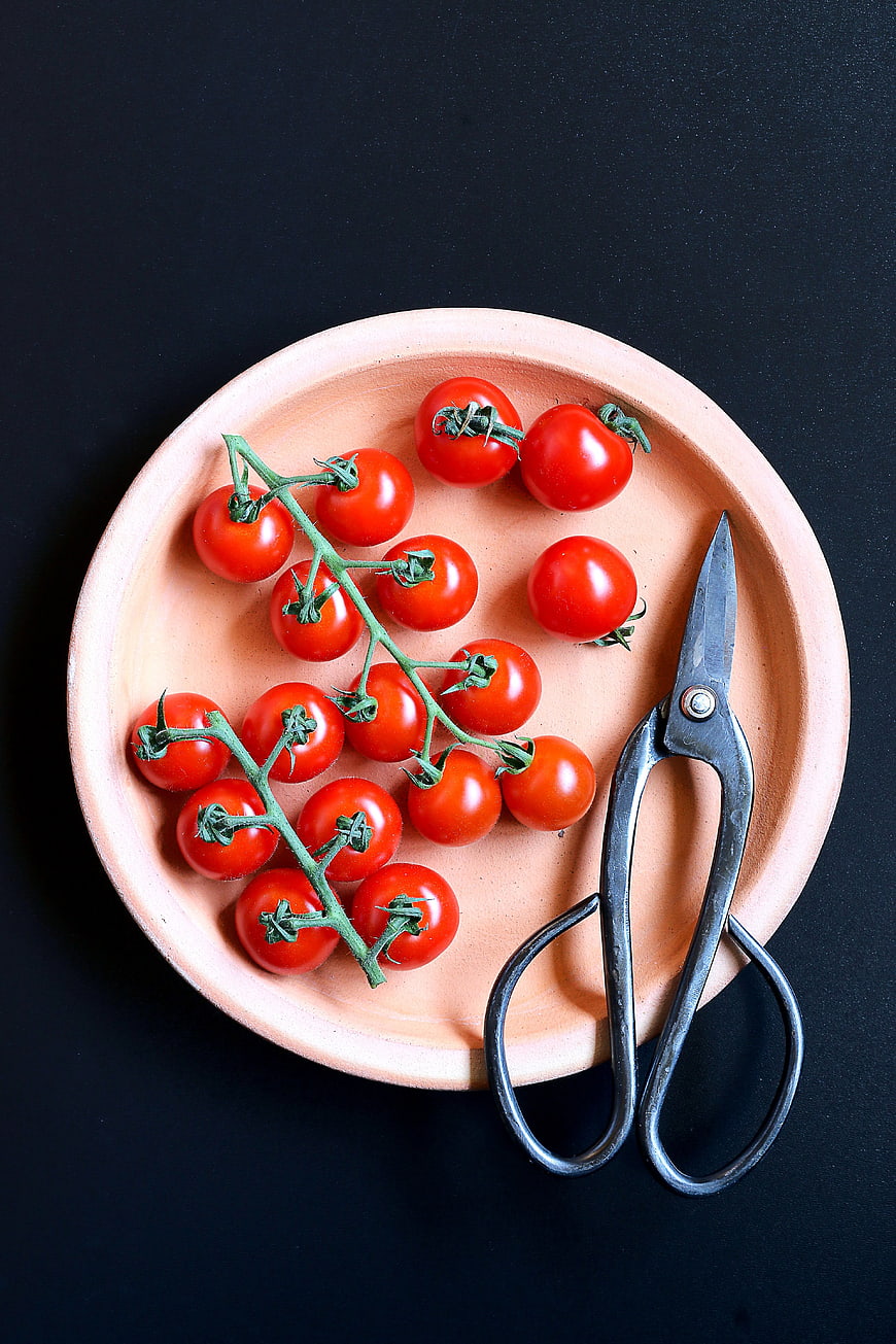 Fresh cherry tomatoes on vine with scissors on wooden plate