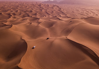 Aerial view of off-road cars driving on vast desert dunes