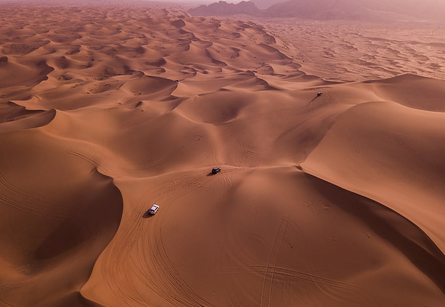 Aerial view of off-road cars driving on vast desert dunes