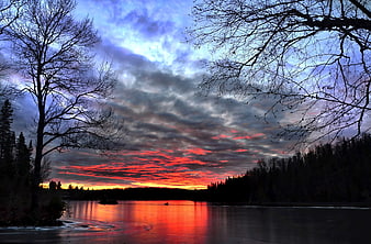 Dramatic red sunset over frozen lake with silhouetted trees