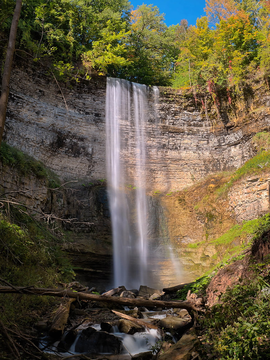 Tall waterfall cascading down rocky cliff in autumn forest