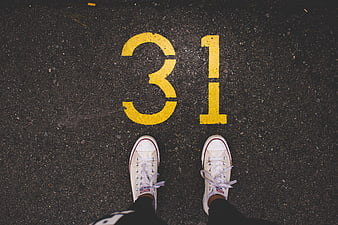 White sneakers standing on asphalt with yellow number 31 painted on the ground