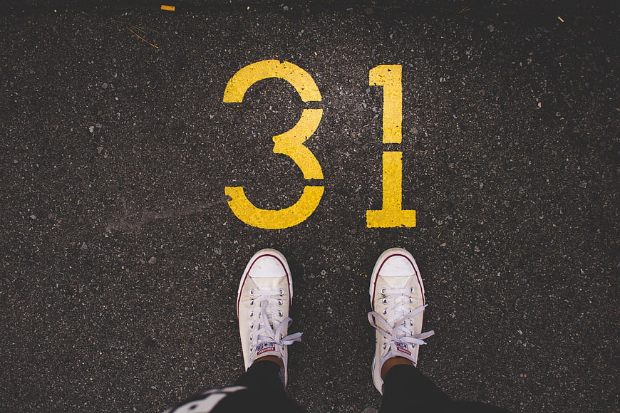 White sneakers standing on asphalt with yellow number 31 painted on the ground