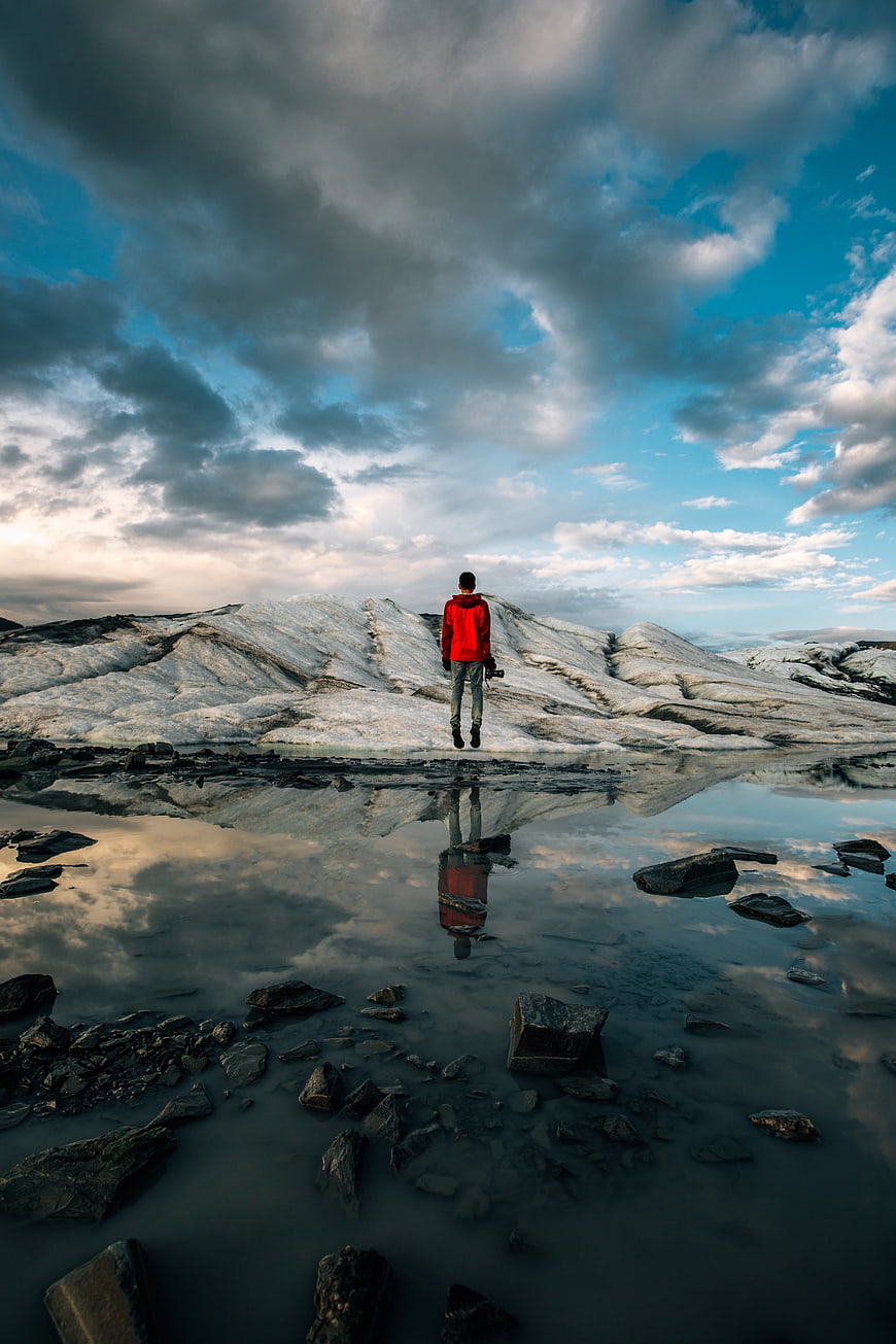 Man in Red Jacket Standing on Glacial Ice with Reflection