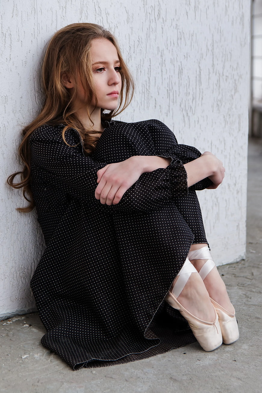 Melancholic Young Woman in Ballet Shoes Sitting Against Wall