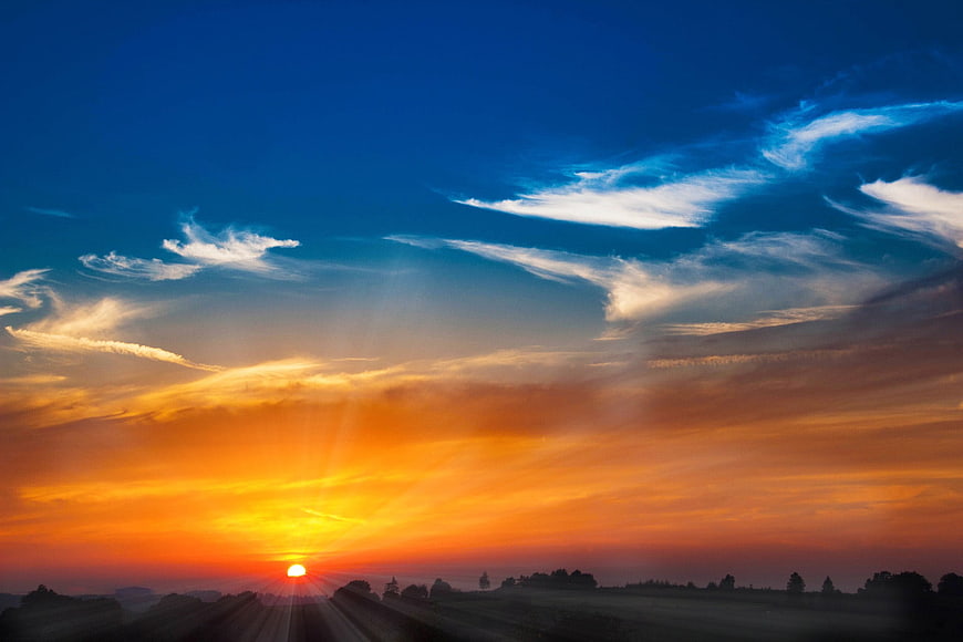 Vibrant sunset with sunbeams over rural landscape silhouette