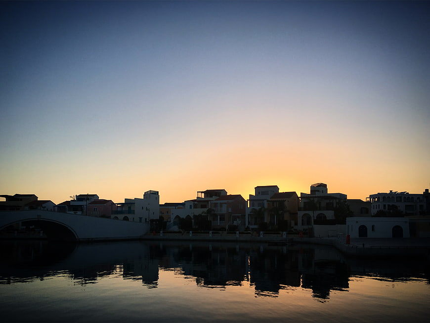 Silhouetted waterfront cityscape at sunset with calm water reflections