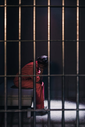 Sad woman in orange jumpsuit sitting in prison cell