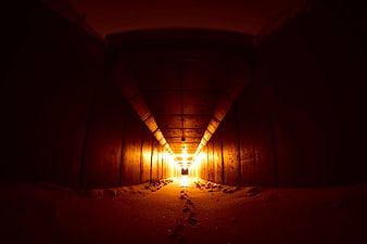 Footprints in sand leading through a dark tunnel to light