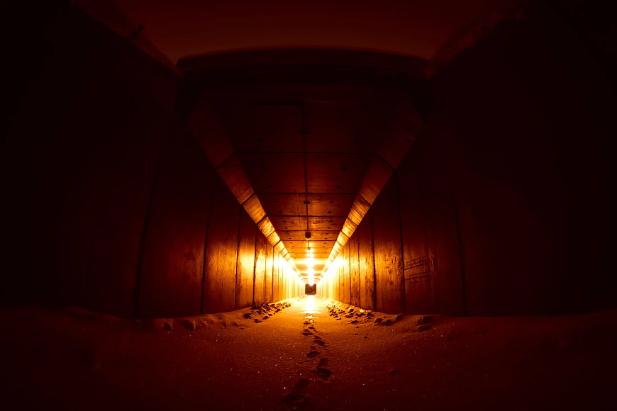 Footprints in sand leading through a dark tunnel to light