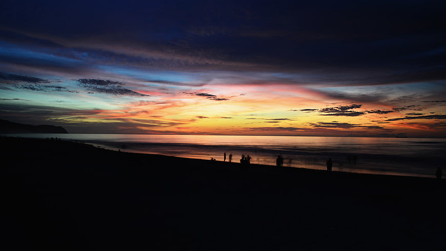 Silhouetted Figures on Beach at Vibrant Sunset