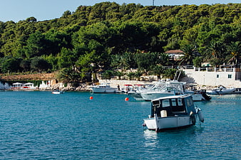 Boats anchored in turquoise Mediterranean harbor with lush green hills