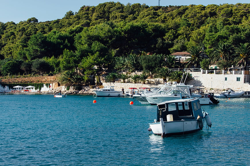 Boats anchored in turquoise Mediterranean harbor with lush green hills