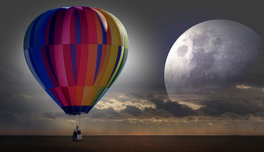 Colorful hot air balloon flying near giant moon over sea