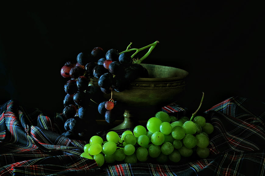 Dark moody still life of green and purple grapes in a bowl