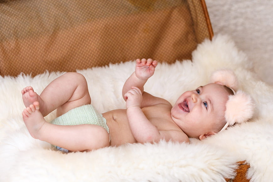 Laughing baby lying on white fur blanket in vintage suitcase