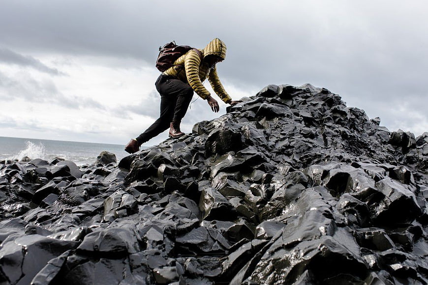 Man Climbing Wet Volcanic Rocks by the Sea