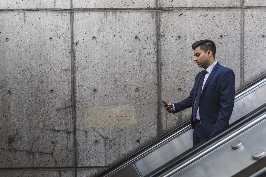 Businessman in Suit Using Smartphone on Escalator