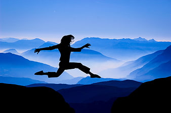 Silhouette of woman jumping between mountains at dusk