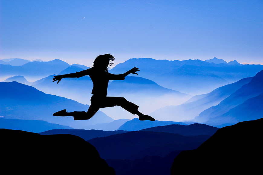 Silhouette of woman jumping between mountains at dusk