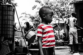 African boy in red striped shirt standing in black and white village setting