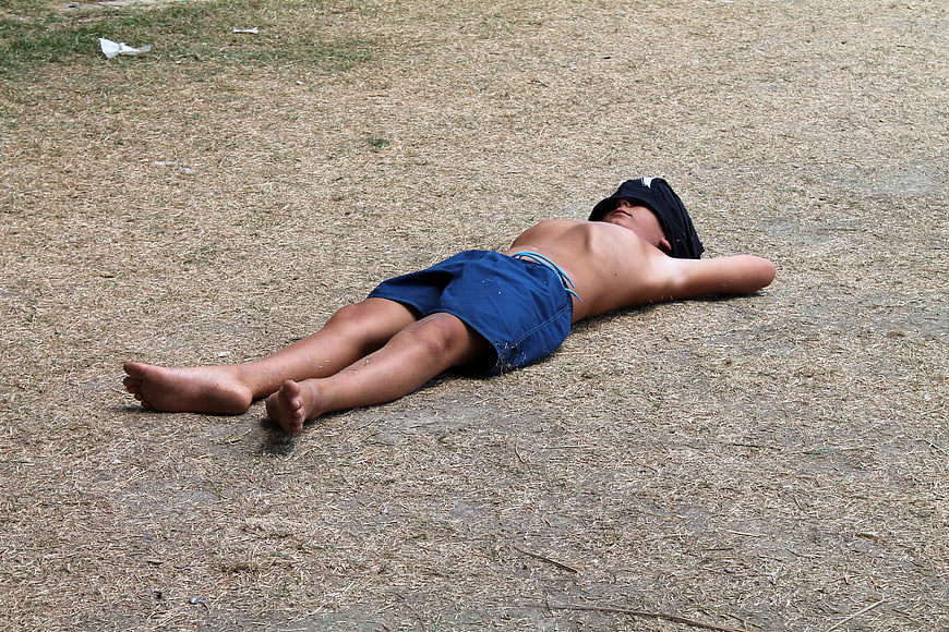 Young man resting on dry grass with shirt over face