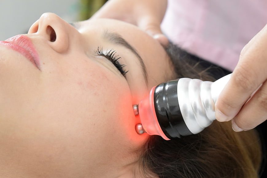 Woman receiving red light therapy facial treatment with device