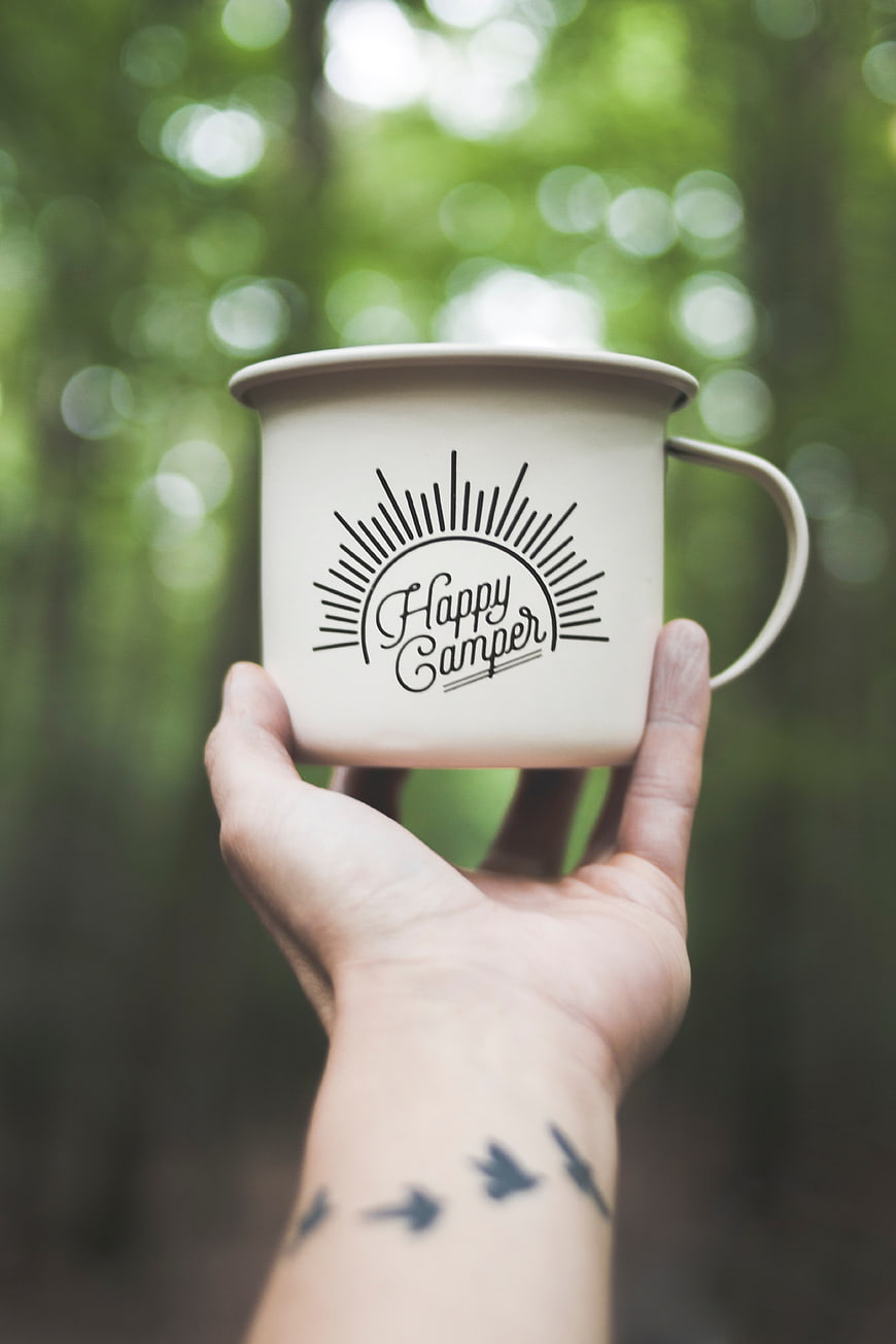 Hand holding Happy Camper mug in forest