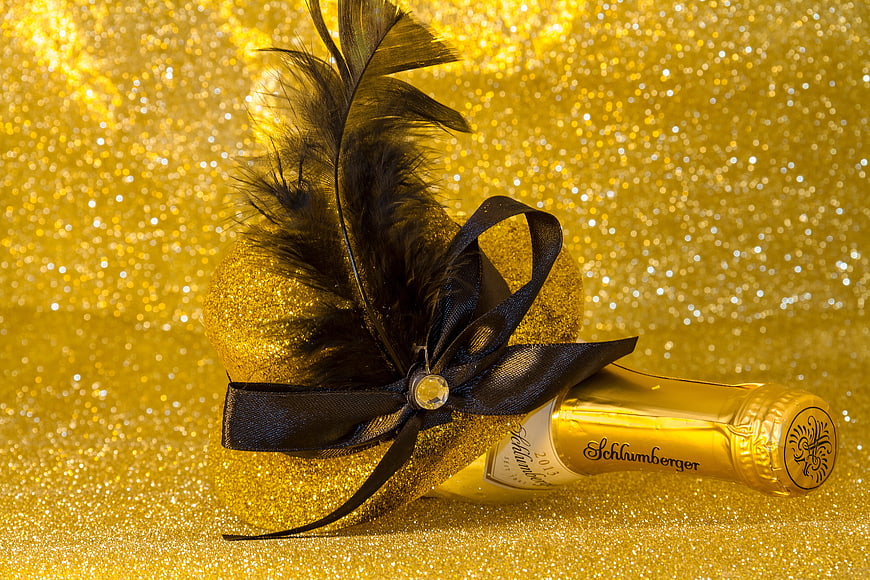Luxury champagne bottle with black feather on gold glitter background