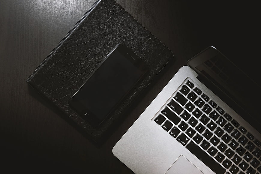 Dark moody workspace with laptop and smartphone on leather notebook