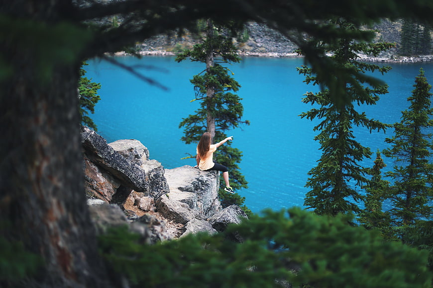 Woman sitting on cliff edge overlooking turquoise alpine lake