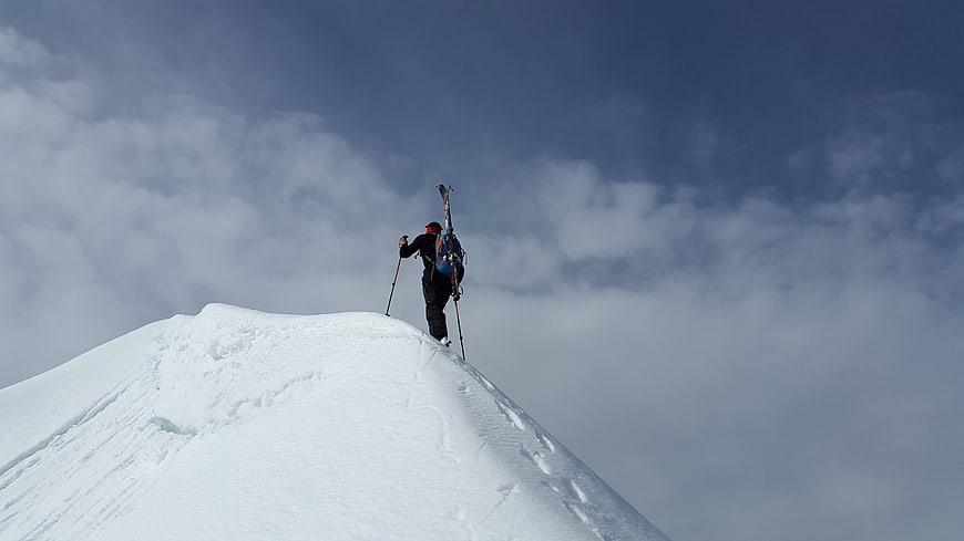 Backcountry skier standing on snowy mountain ridge summit