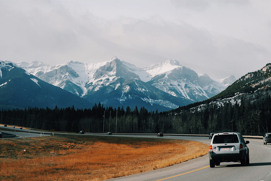 White SUV driving on highway with snowy mountains