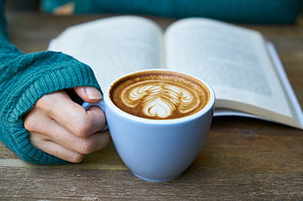 Hand holding coffee cup with latte art and open book