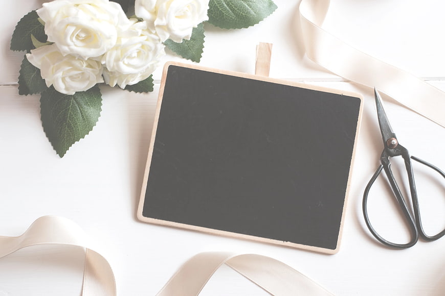 Flat lay of chalkboard, white roses, and scissors on white background