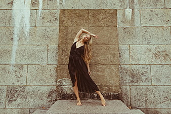 Blonde woman in black dress posing against stone wall
