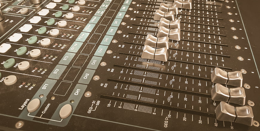 Close-up of professional audio mixing console with sliders and knobs