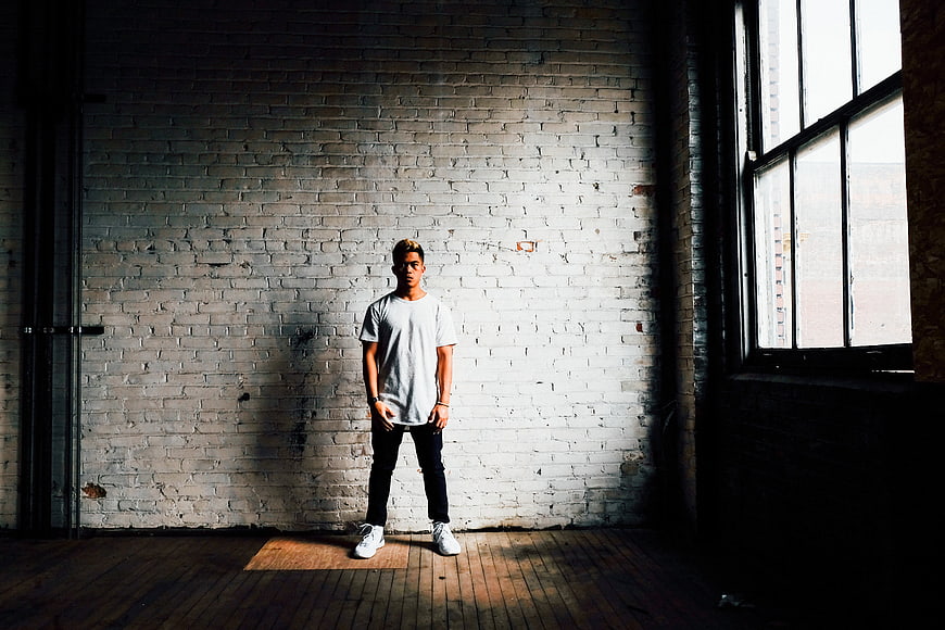 Young man standing in front of white brick wall with window light