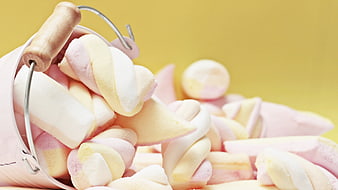 Pink and white marshmallow twists spilling from a pink bucket on yellow background