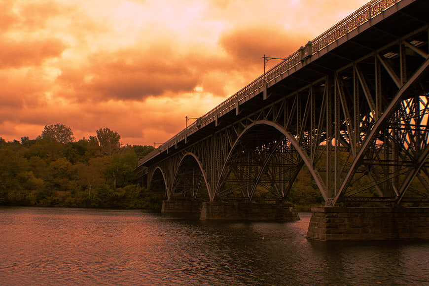 Steel arch bridge over river at dramatic orange sunset