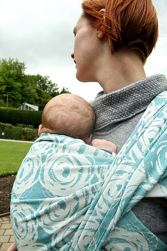 Woman with short red hair carrying newborn baby in woven wrap outdoors