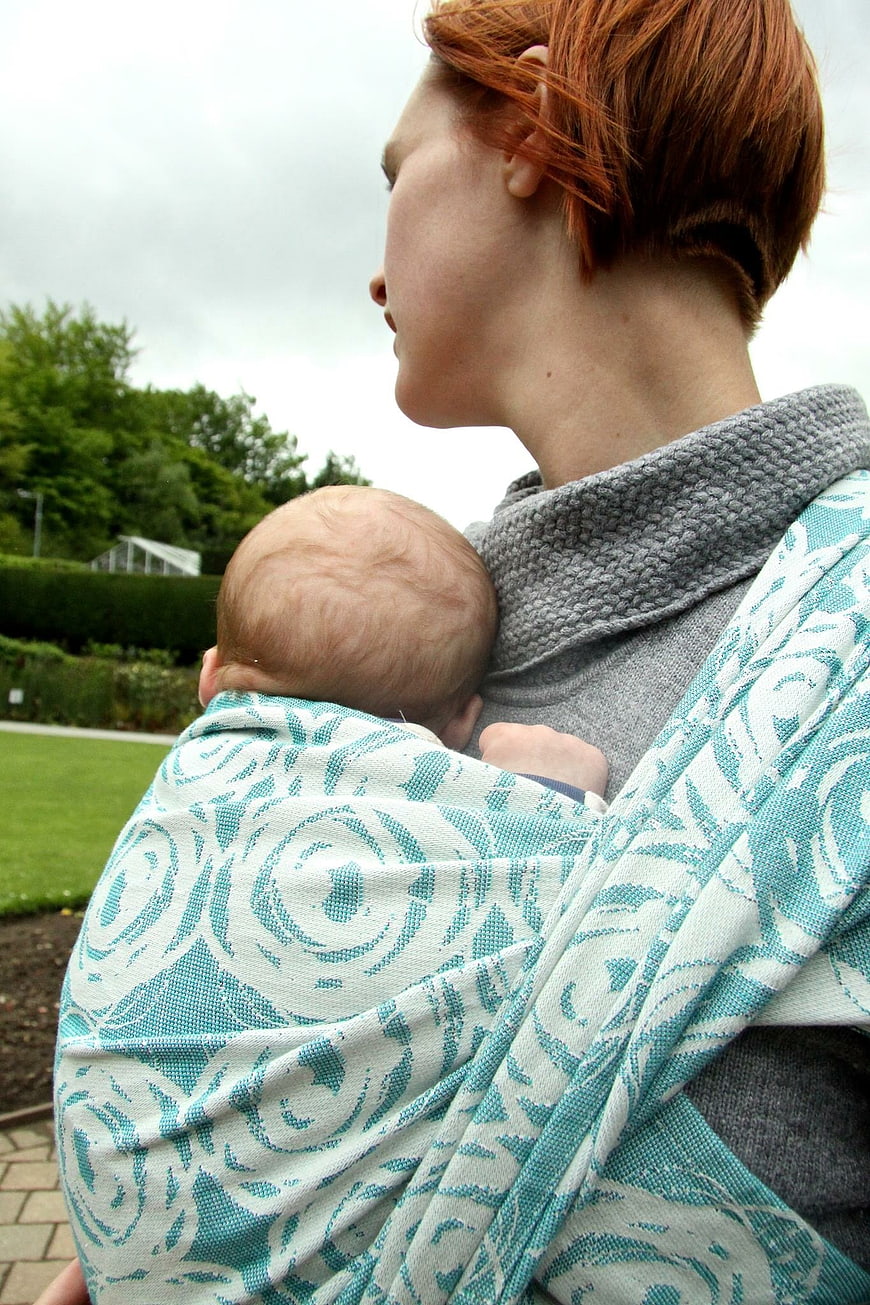 Woman with short red hair carrying newborn baby in woven wrap outdoors